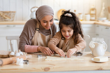 Positive muslim mother and her little daughter preparing cookies together in kitchen