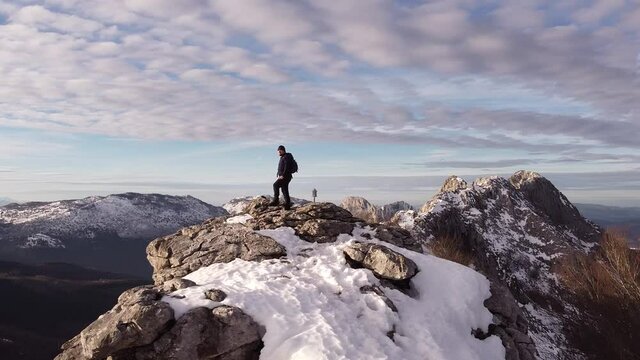 climber reaching a mountain summit in winter (aerial video)