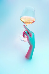 Party time. Close up female hand gesturing from the milk bath with soft white glowing in neon light. Copyspace for advertising. Holding glass of white wine, alcohol. Modern neoned colors.
