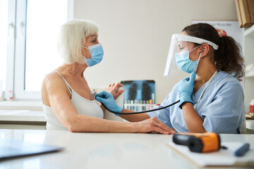 Latin-American medic holding a chest-piece at an old patient breast