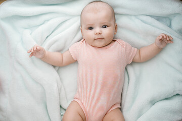 Adorable baby in sunny bedroom. Newborn baby is resting in bed with a warm soft blanket. Family morning at home. Smiling child looking at camera.