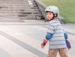 Little Asian Boy is learning to Skate on an Rollerblade in park with full protection gear and...
