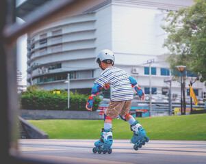 Fototapeta premium Little Asian Boy is learning to Skate on an Rollerblade in park with full protection gear and helmet.
