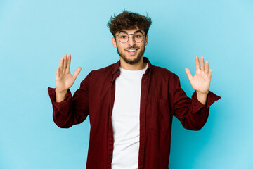 Young arab man on blue background holding something little with forefingers, smiling and confident.