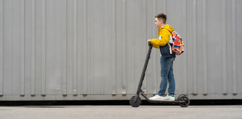 Modern teenager with backpack rides on electric scooter. Boy comes back from school
