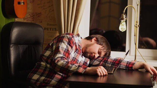a man in red plaid pajamas worked late at the computer and fell asleep.