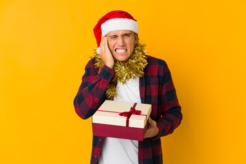 Young caucasian man with christmas hat holding a present isolated on yellow background