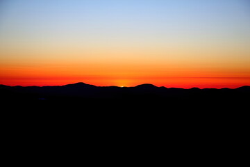 Orange Sunset against black hills and blue sky.