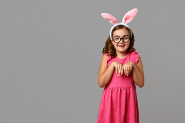Funny cheerful little girl wearing glasses and Easter bunny ears. Child on a gray background.