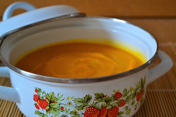 Pumpkin and carrot soup in white pot on wooden background