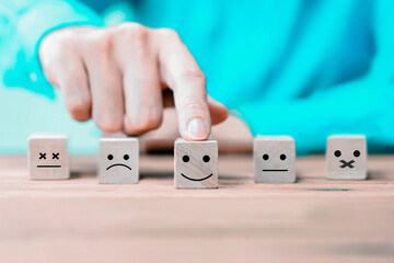 Businessman chooses a happy emoticon icons face on wooden block.