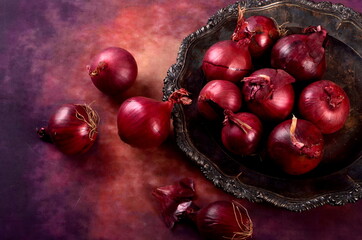 Several red onions on a metal plate, purple background. Still life with red onions