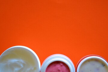 Bottom frame on an orange background made up of three natural cosmetic lotions or creams