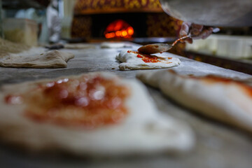 Pizzaiolo mentre stende il sugo di pomodoro su delle pizze ripiene pronte per essere infornate