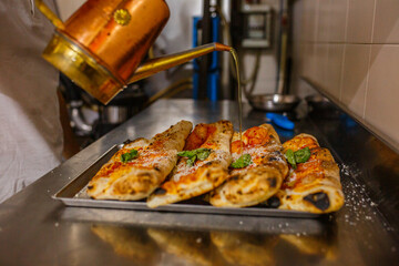 Pizzaiolo mentre mette un filo d'olio su delle pizze ripiene di ricotta e prosciutto