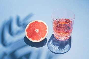 Bright summer drink concept made of crystal glass, palm tree shadow and grapefruit on blue...