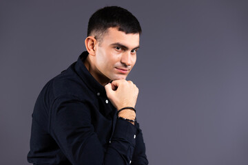 Portrait of a fashionable and serious man in a black shirt looking at the camera on a gray background.