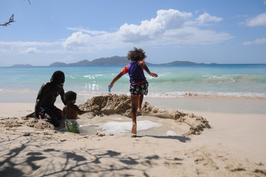 Young Girl Having Fun And Jumping Into A Sea Water Pool On The Beach While Her Father And Brother Is Watching