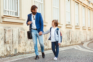 First day at school. Dad leads a son in first grade. Father with kid holding hands at street. Back to school conept.