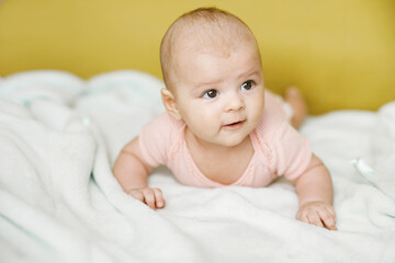 Adorable baby in sunny bedroom. Newborn baby is resting in bed with a warm soft blanket. Family morning at home. Smiling child looking at camera.