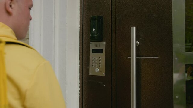 Delivery man walks to intercom or buzzer and dials apartment number on it. Food delivery to the door.
