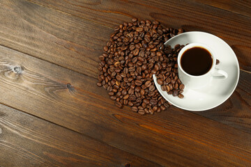 white cup of coffee and coffee beans are on a wooden background. cup of aromatic coffee is on a wooden table with copy space