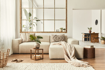 Fototapeta na wymiar Modern interior of open space with design modular sofa, furniture, wooden coffee tables, plaid, pillows, tropical plants and elegant personal accessories in stylish home decor. Neutral living room.
