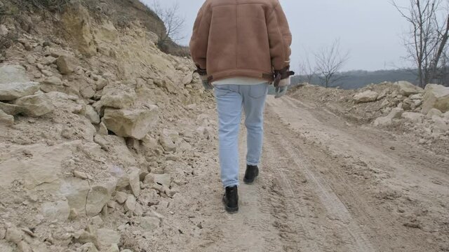 A young guy in a jacket and jeans walks along an abandoned stone carier