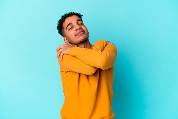 Young african american curly man isolated on blue hugs, smiling carefree and happy.