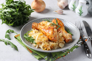 Baked chicken drumsticks with cabbage and garlic on gray plate. Closeup. Horizontal format