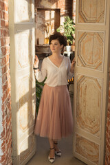 An active, beautiful middle-aged woman. It stands against the background of an old door in the studio. He looks away, smiling.