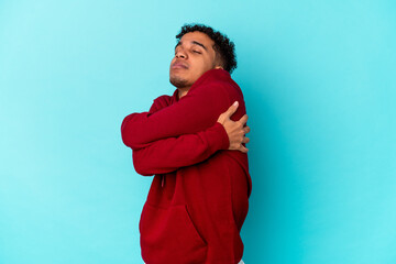 Young african american curly man isolated on blue hugs, smiling carefree and happy.