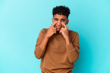 Young african american curly man isolated on blue crying, unhappy with something, agony and confusion concept.