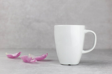 Fototapeta na wymiar Blank white mug mockup with pink tulips petals, light concrete stone background. Valentines, mothers, womens day composition. Side view. Copy space.