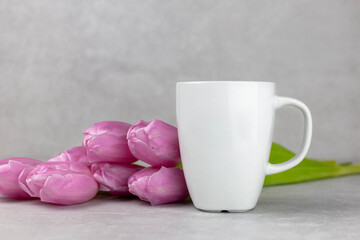 Blank white mug mockup with pink tulips, light concrete stone background. Valentines, mothers, womens day composition. Side view. Copy space.