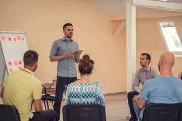 Naklejka premium Group of people listening to a presentation. Man holding tablet and handling the workshop like a pro while speaking on seminar for professional development and team building
