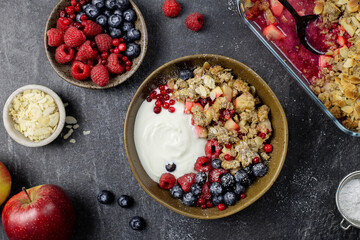 Bowl of homemade granola with yogurt and fresh berries on dark stone concrete background. Cranberry and apple crumble, crisp with almond flakes and oat. Top view.