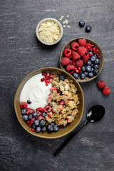Bowl of homemade granola with yogurt and fresh berries on dark stone concrete background. Cranberry and apple crumble, crisp with almond flakes and oat. Top view.