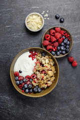 Bowl of homemade granola with yogurt and fresh berries on dark stone concrete background. Cranberry and apple crumble, crisp with almond flakes and oat. Top view.