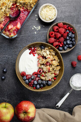Bowl of homemade granola with yogurt and fresh berries on dark stone concrete background. Cranberry and apple crumble, crisp with almond flakes and oat. Top view.