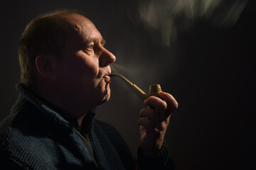 Fototapeta premium Nice portrait of a Caucasian man with tobacco pipe (side view, low key)