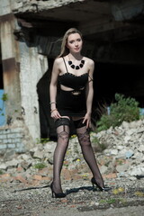 Fototapeta na wymiar Beautiful sexy blonde girl in a black dress and stockings posing on a background of ruins