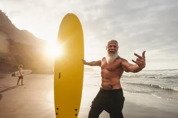 Fotobehang Happy fit senior having fun surfing at sunset time - Sporty bearded man training with surfboard on the beach - Elderly healthy people lifestyle and extreme sport concept © Alessandro Biascioli