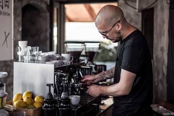 Handsome and urban young tattooed man making coffee on coffee machine in cafe. Young barista is making a coffee.