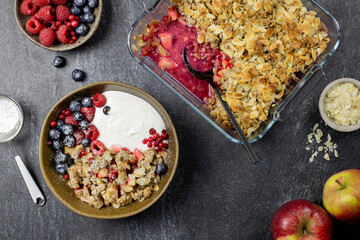 Cranberry and apple crumble, crisp in a glass baking dish with almond flakes and fresh berries on dark stone concrete background. Top view.