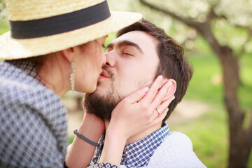 A young girl in a straw hat kisses a guy. Loving couple in the garden.