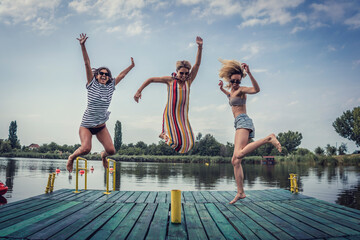 Group of three happy female friends enjoying summertime and beautiful day outdoors at river lake, having fun, jumping and laughing