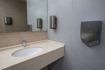 Bathroom with white washbasin and taps. Public restroom interior. Large mirror, dry towels,...