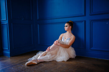 Fototapeta premium Young dancer sitting in a dance studio near a blue wall and resting