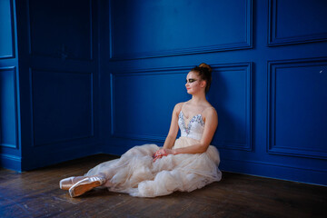 Fototapeta premium Young dancer sitting in a dance studio near a blue wall and resting